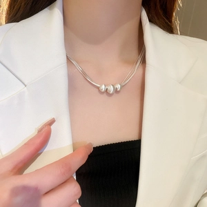 Nahaufnahme von drei weißen Rundperlen an einer silbernen Mehrschichtkette am Model