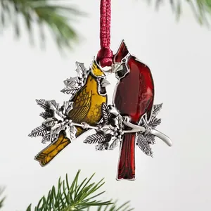 Silver metal cardinal ornament with red enamel details hanging on a Christmas tree branch