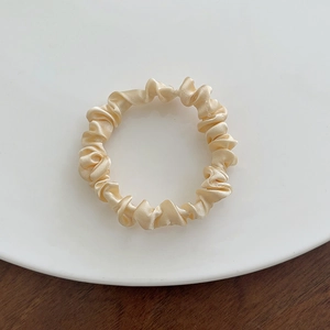 Close-up of a beige satin scrunchie with pleated texture on a white ceramic plate