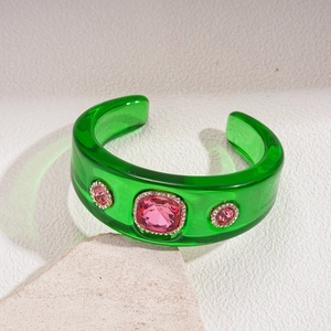 Detail of translucent green resin cuff featuring pink crystal inlay and gold trim
