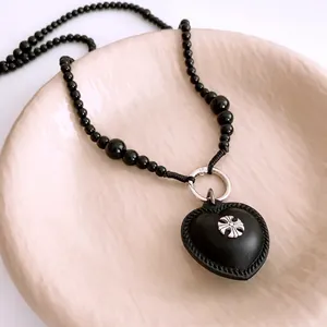 Beaded necklace with black leather heart pendant and silver cross emblem in a ceramic dish