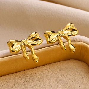 Polished gold bow stud earrings on a beige velvet jewelry box tray for women