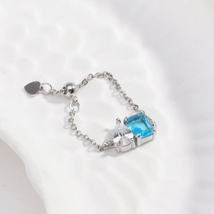 Detail of adjustable silver ring with emerald-cut blue and drop-shaped clear zircons
