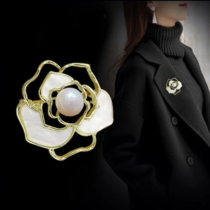 Detail of camellia brooch with white petals, gold trim and pearl on black background