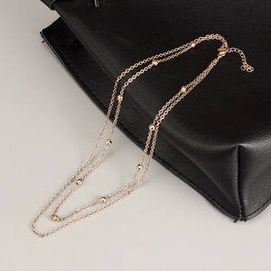 Detail of rose gold double-layered beaded necklace on black leather surface