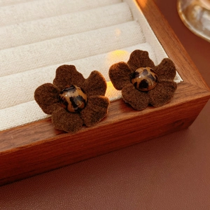 Macro detail of plush brown flower earrings with leopard print beads on wood tray