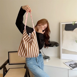 Detail of striped canvas tote bag featuring pink ruffled handles and spacious bottom