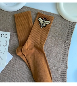 Detail of tan ribbed crew socks featuring a golden embroidered bee patch decoration