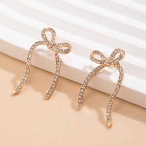 Detailed close-up of golden bow earrings with sparkling rhinestones on a display stand