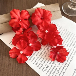 Macro detail of red fabric flower earrings with pearls and golden chain accents