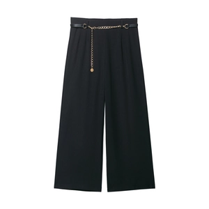 Dettaglio dei pantaloni neri a vita alta con cintura a catena dorata e tessuto sartoriale