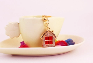 Close-up of golden house keychain with red crystals hanging on a yellow teacup