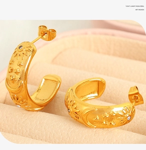 Macro shot of gold C-shaped earrings with celestial sun and moon relief patterns