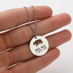 Detailed close-up of MAMA bear engraved round pendant necklace held in hand to show scale