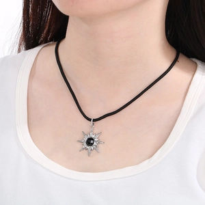 Detail of silver sunburst pendant with black gemstone on a cord necklace worn by model