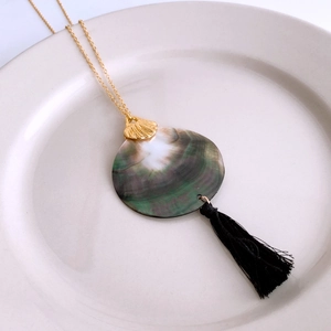 Detail view of iridescent shell pendant with golden clasp and black fringe tassel necklace