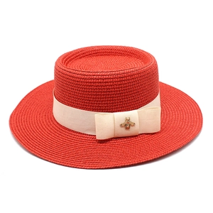 Detail of red boater hat straw weave with cream ribbon and gold bee ornament