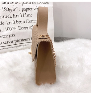 Detail view of beige textured crossbody bag with gold twist lock and chain strap