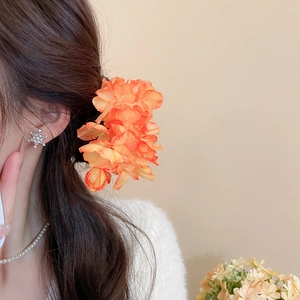 Detail view of handmade orange fabric flower hairpin styled on elegant model