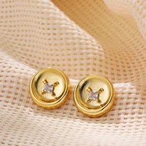 Macro shot of 18K gold button earrings with square cubic zirconia on white woven fabric