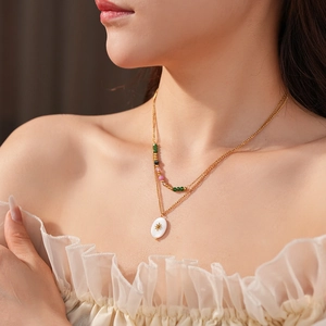 Detailed view of layered gold necklace with colorful beads and white sunburst oval pendant