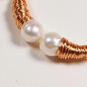 Macro detail of white freshwater pearls and golden wire wrap on a double-layer bracelet