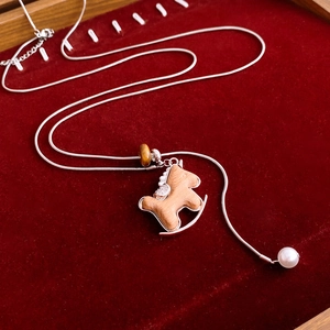 Macro shot of a wooden rocking horse pendant on a silver snake chain with tiger eye bead