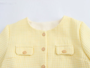 Close-up of yellow tweed jacket with round neck and detailed gold buttons on pockets