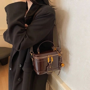 Brown mirror leather box bucket bag with golden zipper and woven charm shown on model