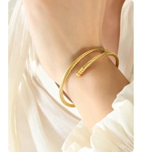 Detailed view of a gold cable motif open bangle with textured spiral and bead ends