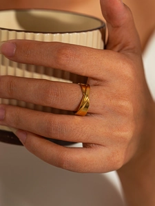 Detailed view of a gold twist ring with matte finish worn on a finger holding a ceramic cup