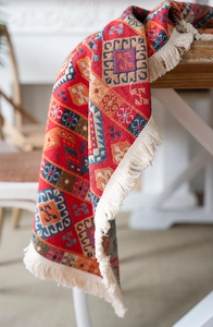 Detail of red jacquard ethnic tablecloth with colorful geometric patterns and beige tassels