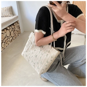 Detail of cream straw tote bag featuring green leaf embroidery and lace bow decoration