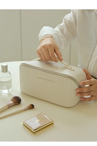 Macro shot of cream leather makeup bag with gold zipper and top handle on a white desk