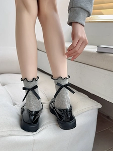 Detail of grey socks with black ruffle trim and decorative ribbon bow on the back