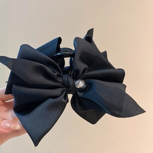 Detail of a large black satin bow hair claw clip featuring a crystal center on a beige base