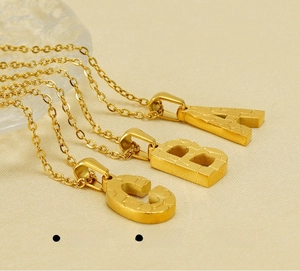 Macro shot of 18K gold plated stainless steel A, B, C alphabet pendants with textured finish