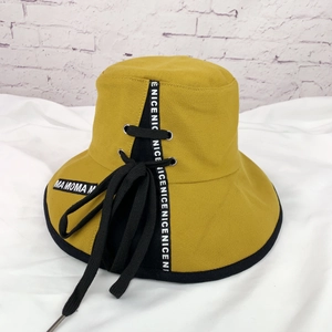 Détail d'un chapeau bob jaune gingembre avec lanières noires et imprimé NICE blanc