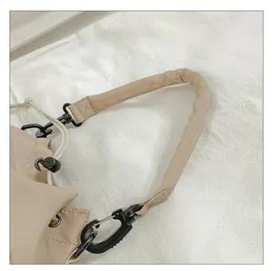 Detail showing padded beige nylon shoulder strap with matte black lobster clasp hook