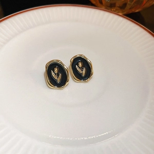 Detail view of black enamel tulip earrings with gold plated irregular edges on white plate