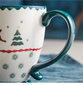 Macro detail of Christmas ceramic mug featuring green tree prints and snowflake patterns