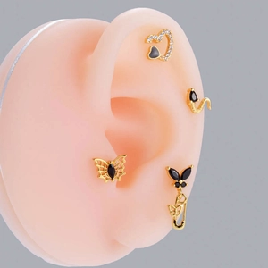 Macro shot of gold butterfly and black heart stud earrings on a silicone ear model