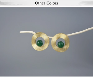 Artistic display of geometric gold earrings with deep green stones on a white twig branch
