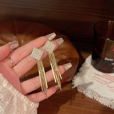 Detail view of long gold tassel earrings with square rhinestone studs in hand