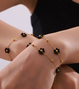Gros plan d'un bracelet doré avec perles fleurs noires sur le poignet d'un modèle