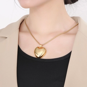 Close-up of golden hollow heart pendant necklace worn on neck with snake bone chain