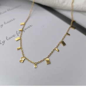 Macro shot of minimalist gold teardrop necklace with small rectangular polished pendants