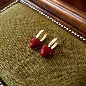 Vue macro de boucles d'oreilles cœur rouge plaquées or sur un tissu vert texturé vintage