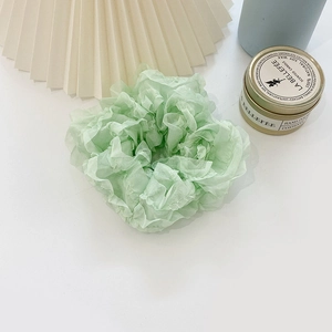 Close-up of light green ruffled scrunchie with soft fabric texture on white background