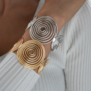 Detailed view of gold and silver spiral cuff bracelets on a model with metallic texture
